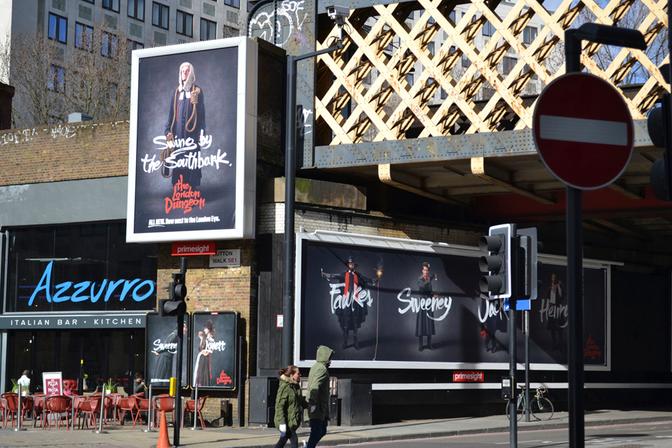 A billboard for the London Dungeon featuring a large image of a woman in a Victorian-era style dress, with a sign in the background reading 'The London Dungeon' and a large image of a man in a Victorian-era style dress, with a sign in the background reading 'The London Dungeon'