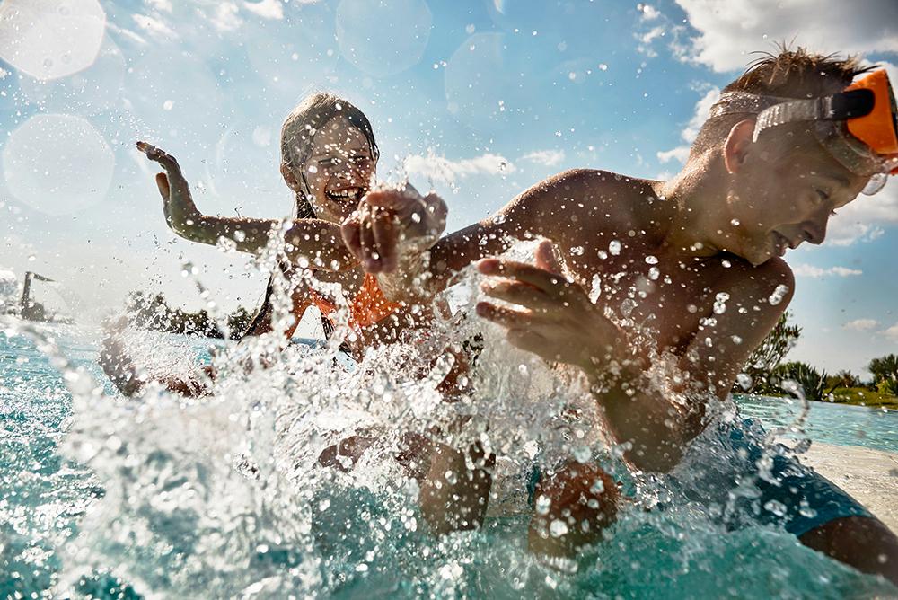 Two young boys in swimwear and snorkeling gear playing in the water, splashing and having fun.