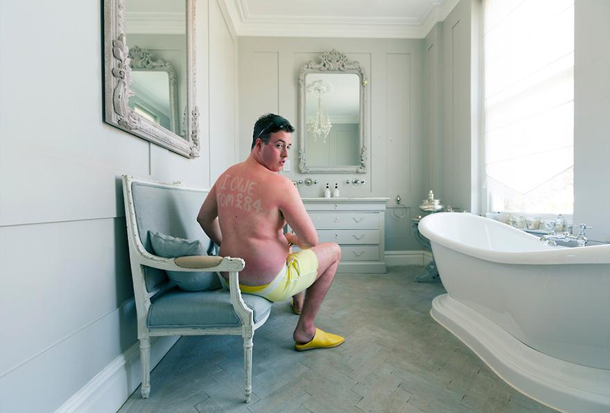 A man sits on a chair in a bathroom with sunburned back and letters.