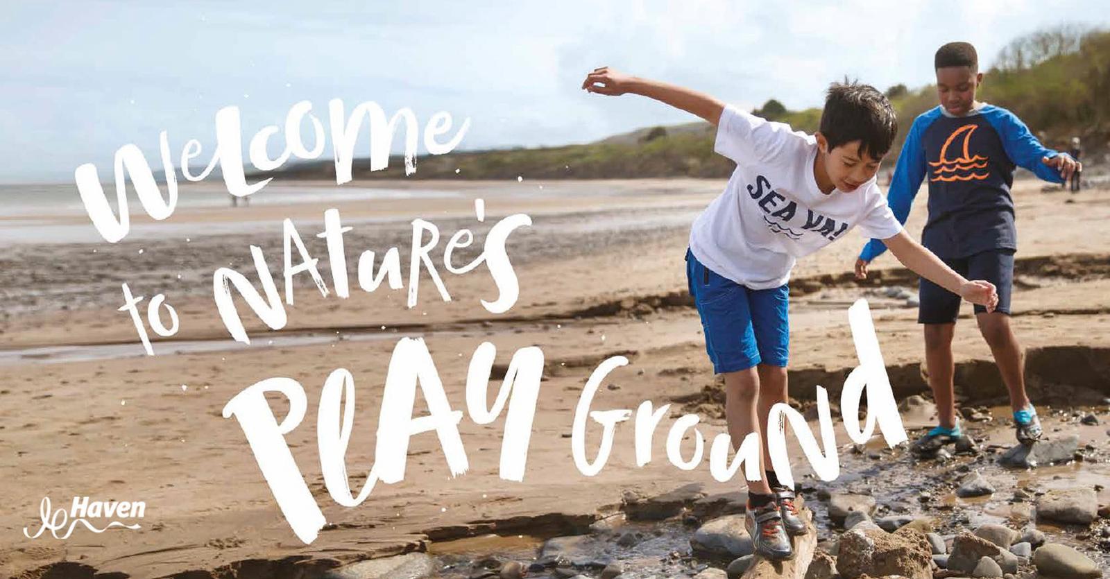 Two children playing on a beach. The boy in the white t-shirt is jumping over rocks, while the boy in the blue t-shirt is watching him. They seem to be enjoying themselves.