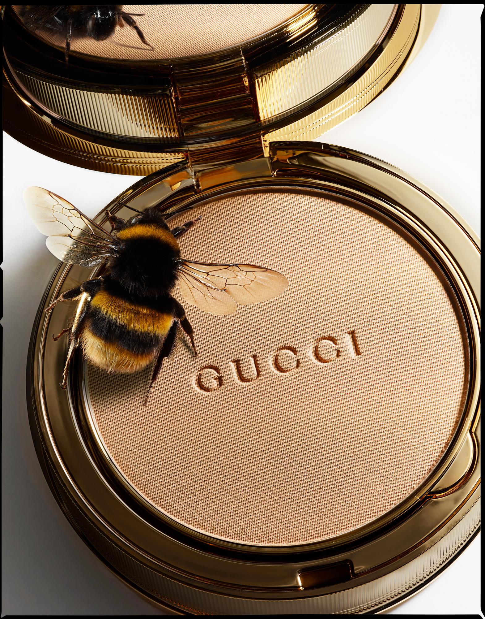 A compact powder compact with a gold lid, featuring a large, golden-brown, furry bee on top, with its wings spread out.