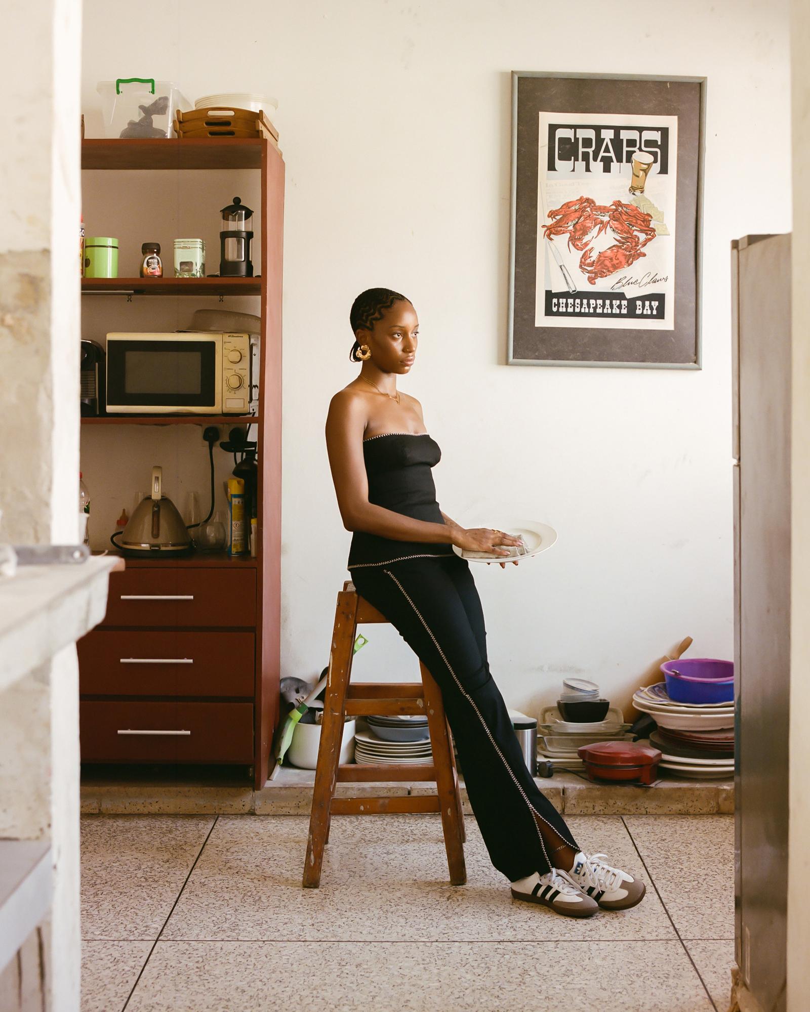 A woman sits on a stool in a kitchen holding a plate.