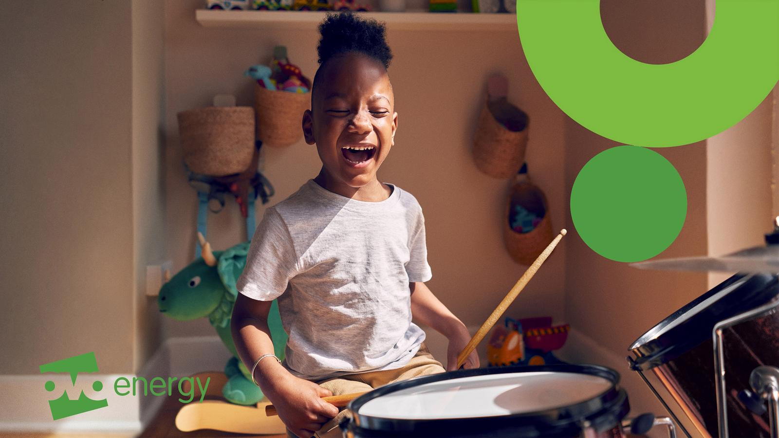 A young boy playing a drum set in a playroom with toys and a shelf in the background.