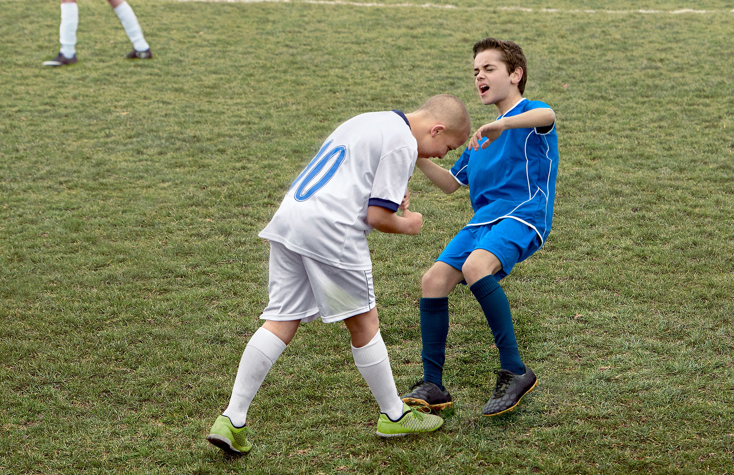 Two young boys in soccer uniforms playing soccer on a grassy field.