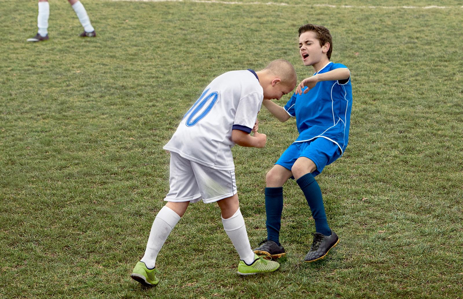 Two young boys in soccer uniforms playing soccer on a grassy field.