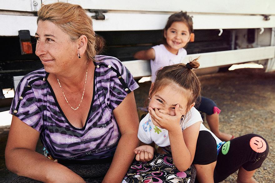 A woman and two young girls sitting on the ground, with the woman wearing a purple and black striped shirt and the girls wearing white and black tops and black pants.