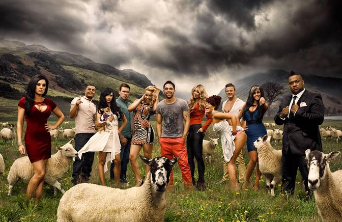 A group of people, including celebrities, posing in a field with sheep in the background, with mountains and a cloudy sky.