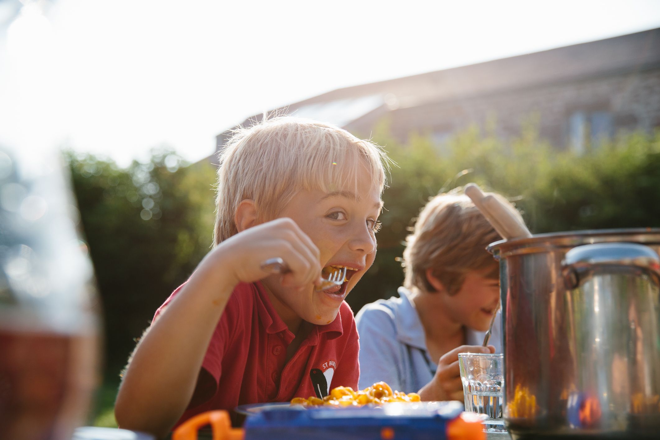 Two boys eating spaghetti in a garden.
