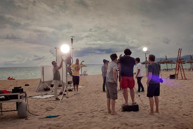 A group of people on a beach, some with cameras and lighting equipment, setting up for a photo shoot.