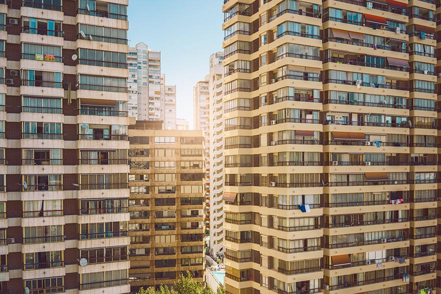 A densely populated urban landscape with numerous high-rise buildings and apartments, with some windows and balconies visible.