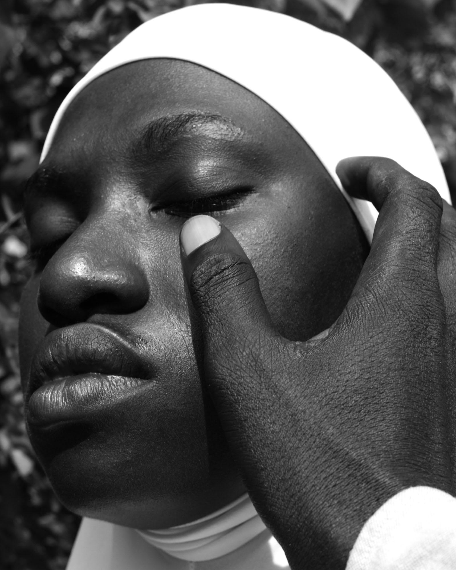 A close-up of a person's face, with a white headscarf covering their hair, and a hand gently touching their cheek.