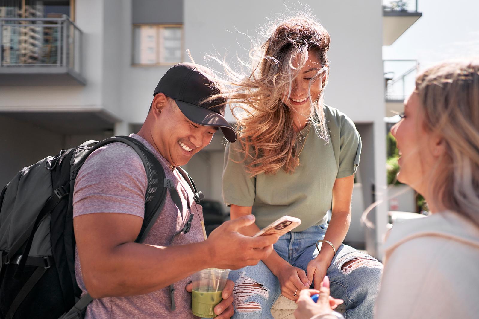 A man and two women laugh while standing on a city street.