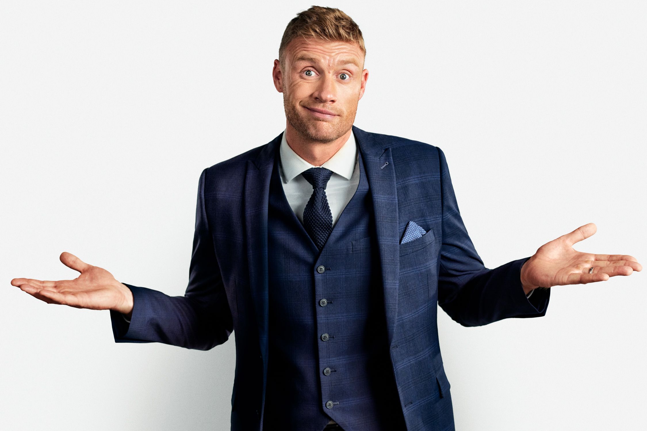 A man in a navy blue three-piece suit with a white shirt and a navy blue tie, looking directly at the camera with a surprised expression.