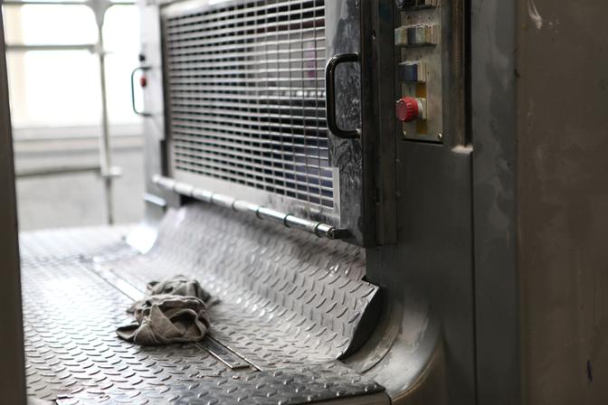 A worn, grey, industrial-style, metal floor mat with a few scattered, dirty, grey rags.