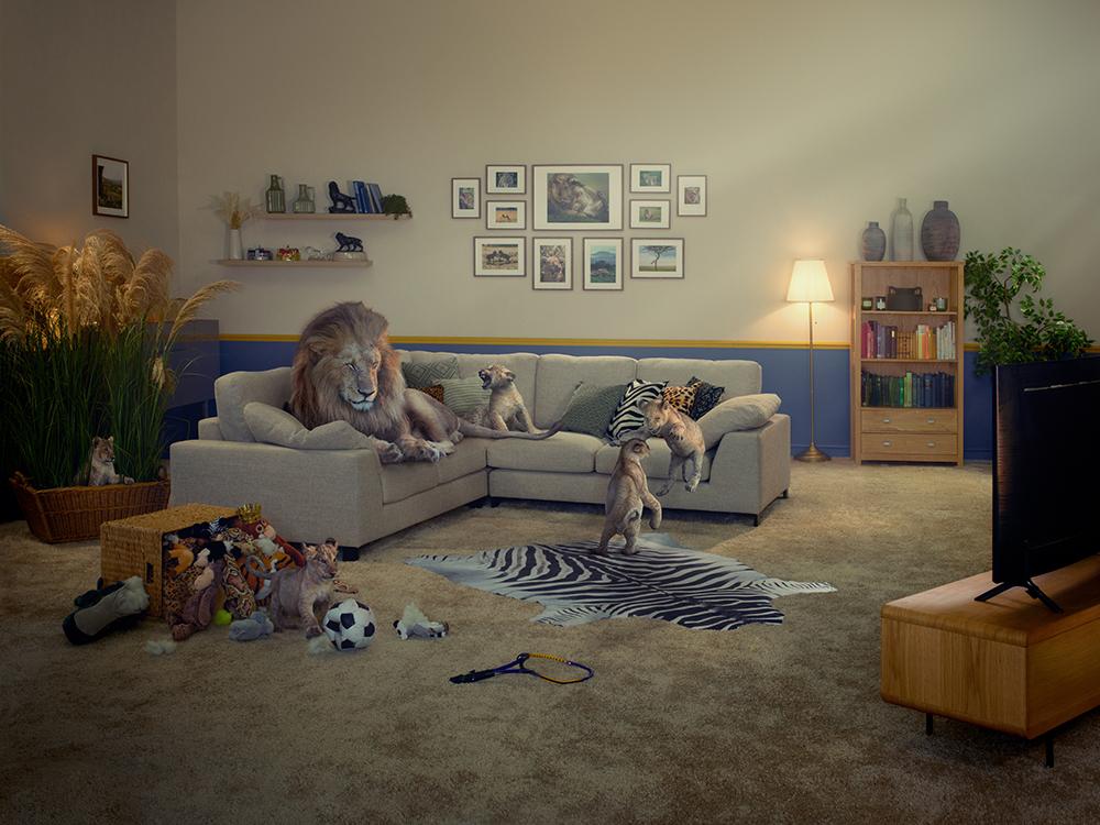 A living room with a couch, TV, and a lion among other animals and toys, featuring a zebra skin rug.