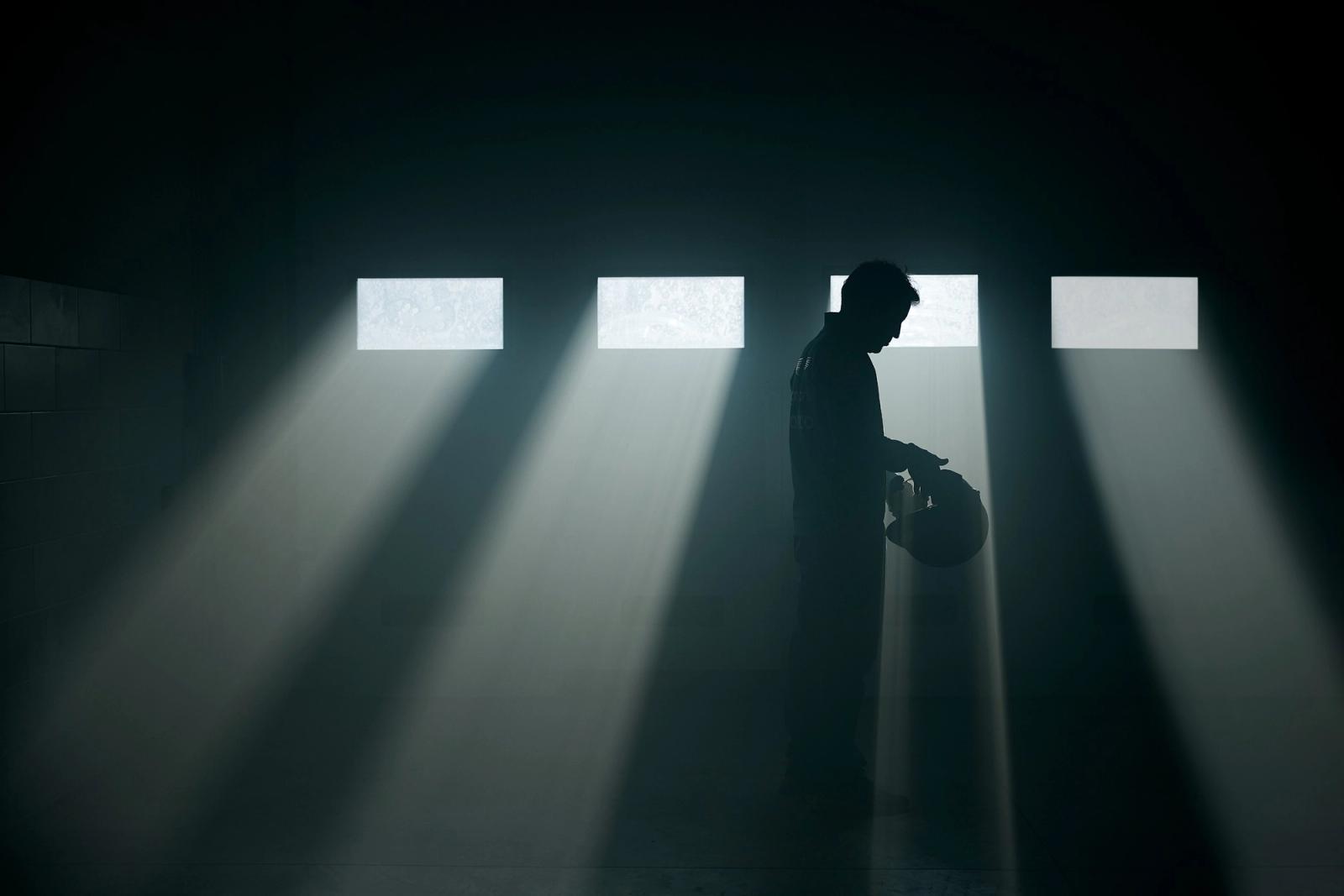 A man in a football jersey stands in a dimly lit room, surrounded by spotlights, holding a football.