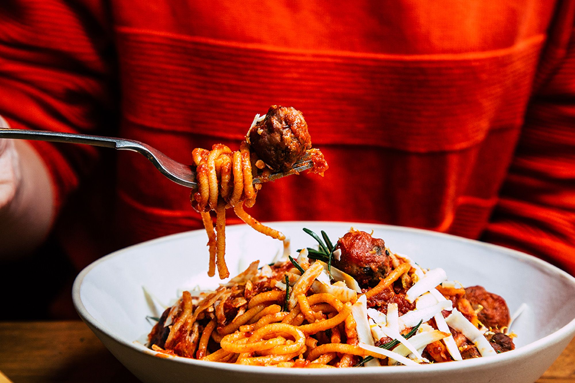 A person is eating a plate of spaghetti with a fork, with a red background.