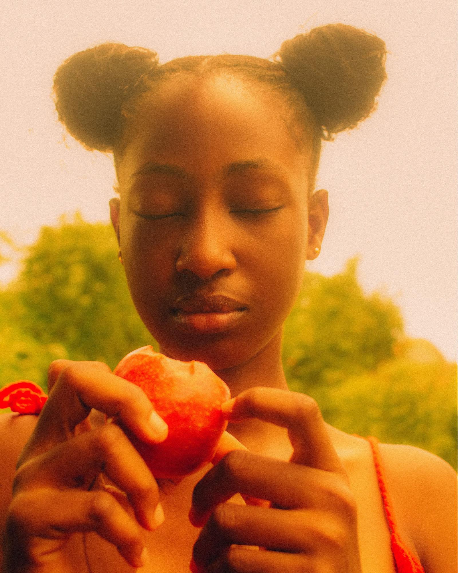 A young woman with her eyes closed, holding a peach in her hands, with a serene and peaceful expression.