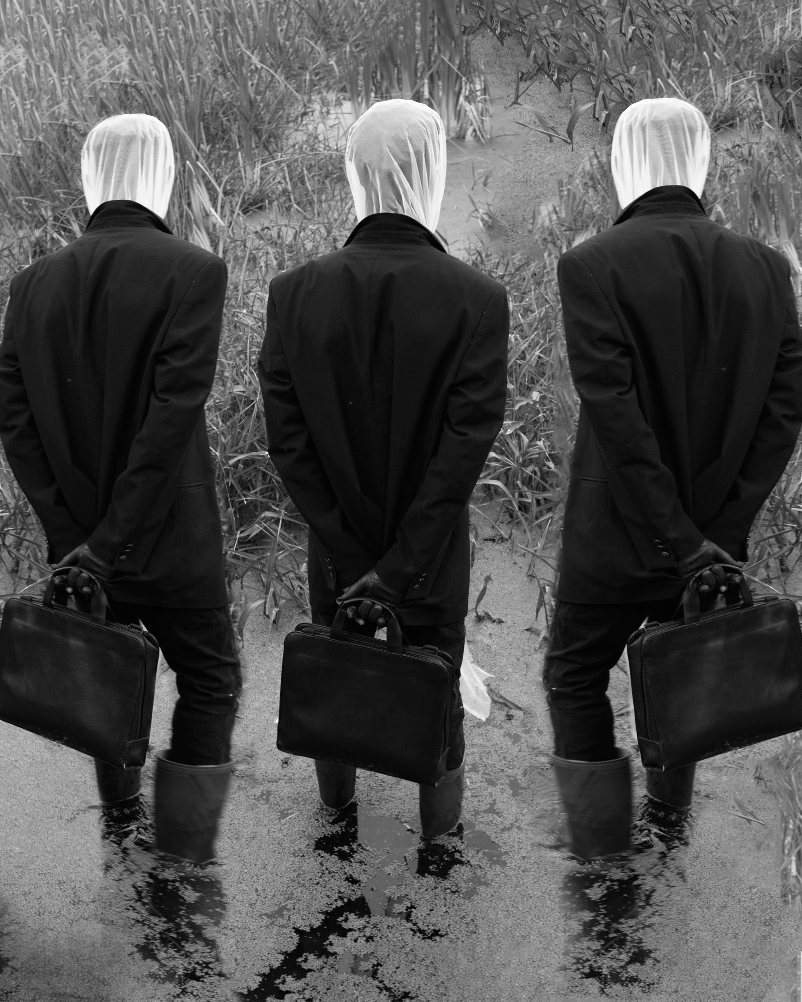 Three figures in black suits with white masks carrying briefcases in a field.