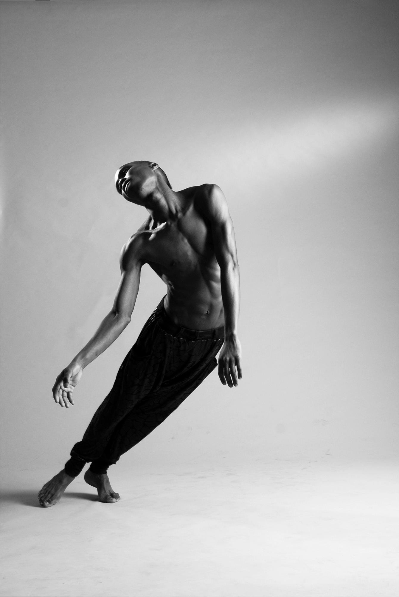 A male dancer in a dynamic, abstract pose, wearing a black dance costume, with a focus on his athletic physique and expressive movement.
