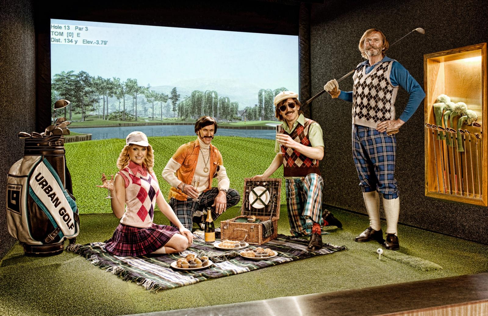A group of people wearing 1970s-style golfing attire have a picnic on a golf course with golfing equipment in the background.
