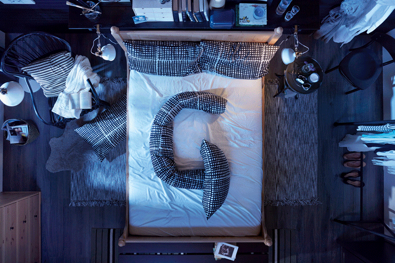 A person is sleeping in a bed with a white sheet and a few pillows, surrounded by a dark and cozy atmosphere.