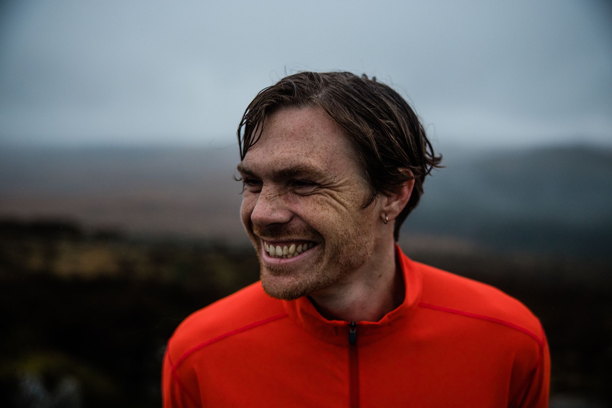 A man with a red jacket and a wide, toothy grin, looking directly at the camera with a sense of joy and contentment.