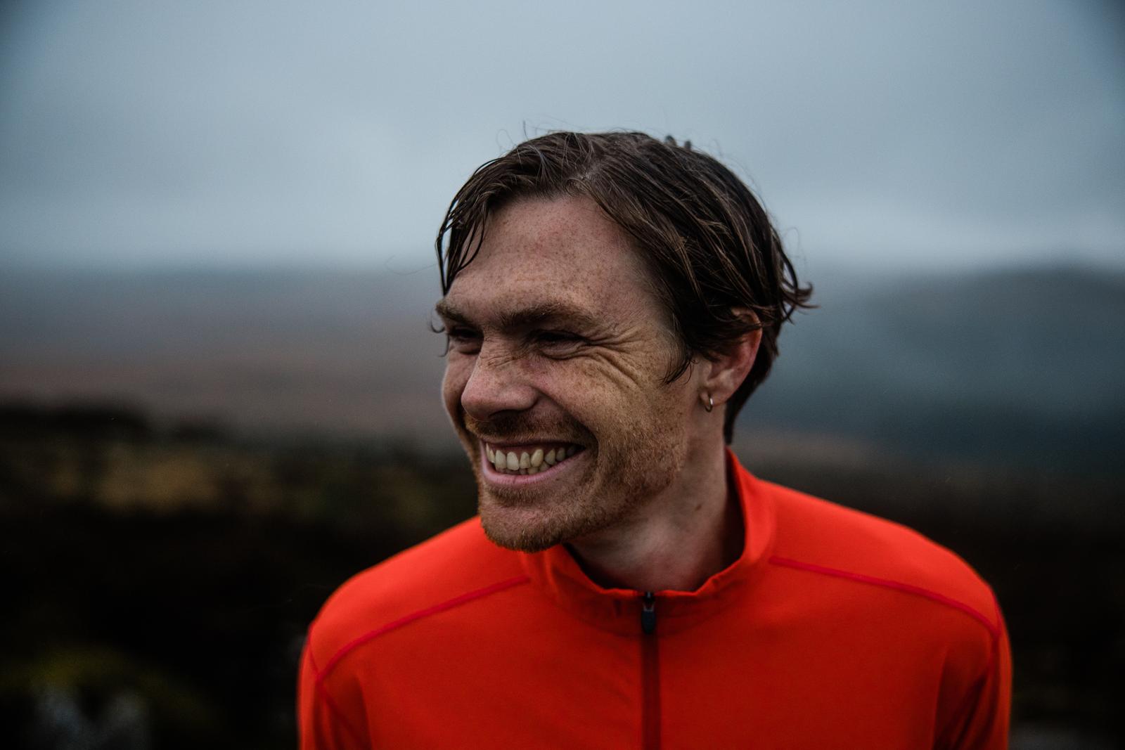 A man with a red jacket and a wide, toothy grin, looking directly at the camera with a sense of joy and contentment.
