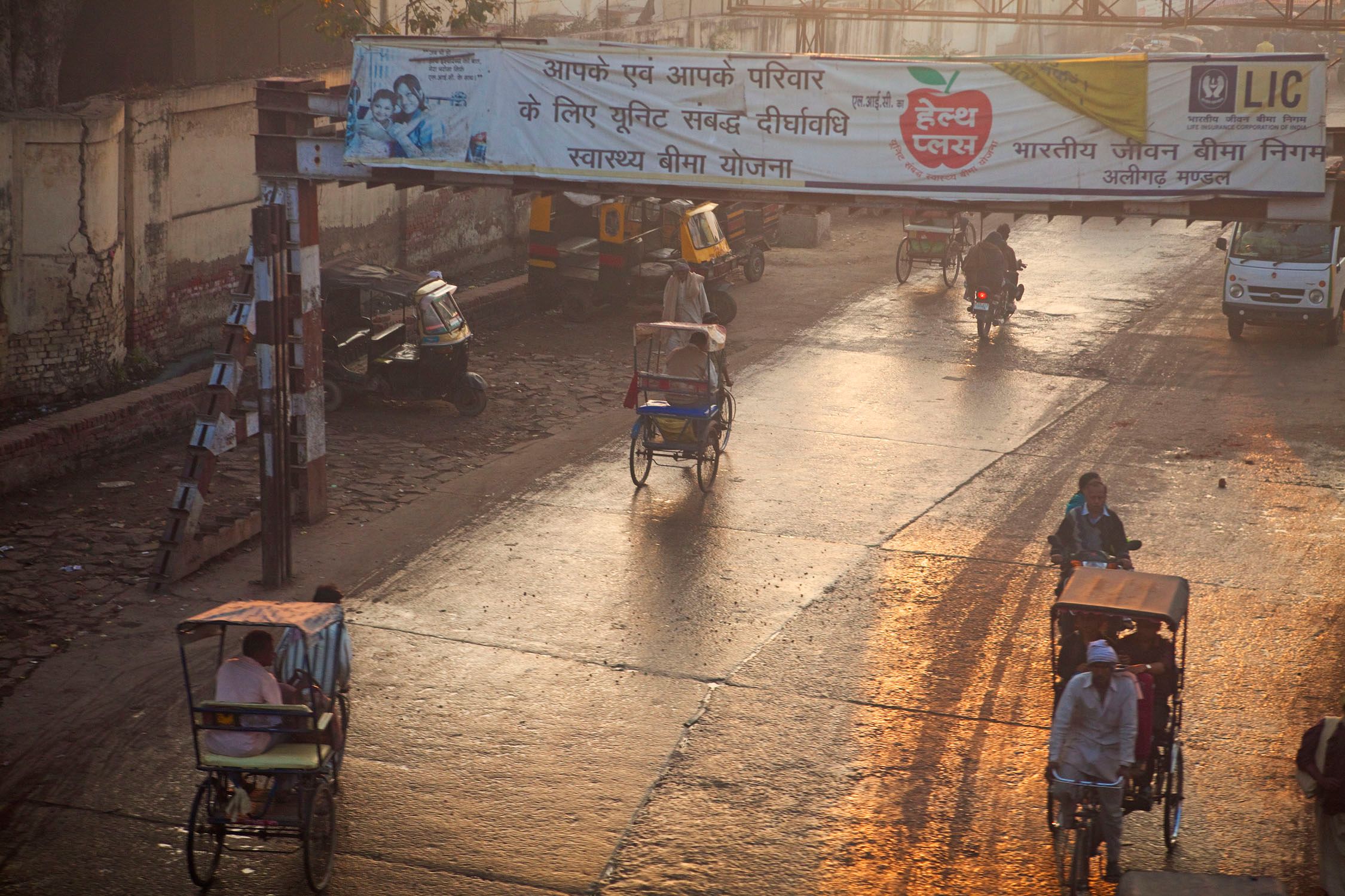 A street scene with rickshaw drivers and a large banner featuring Indian text and a red apple logo.