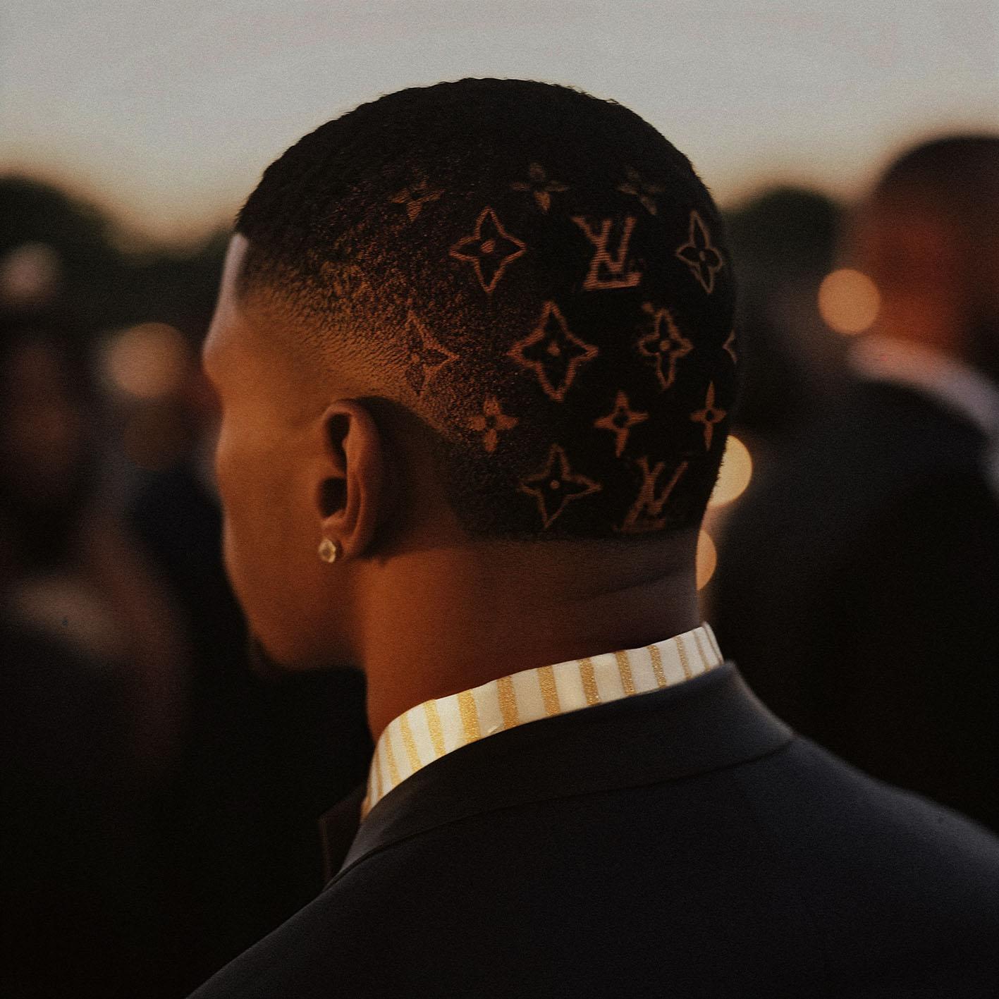 A close-up of a man’s head with a shaved design featuring the Louis Vuitton logo and other patterns.