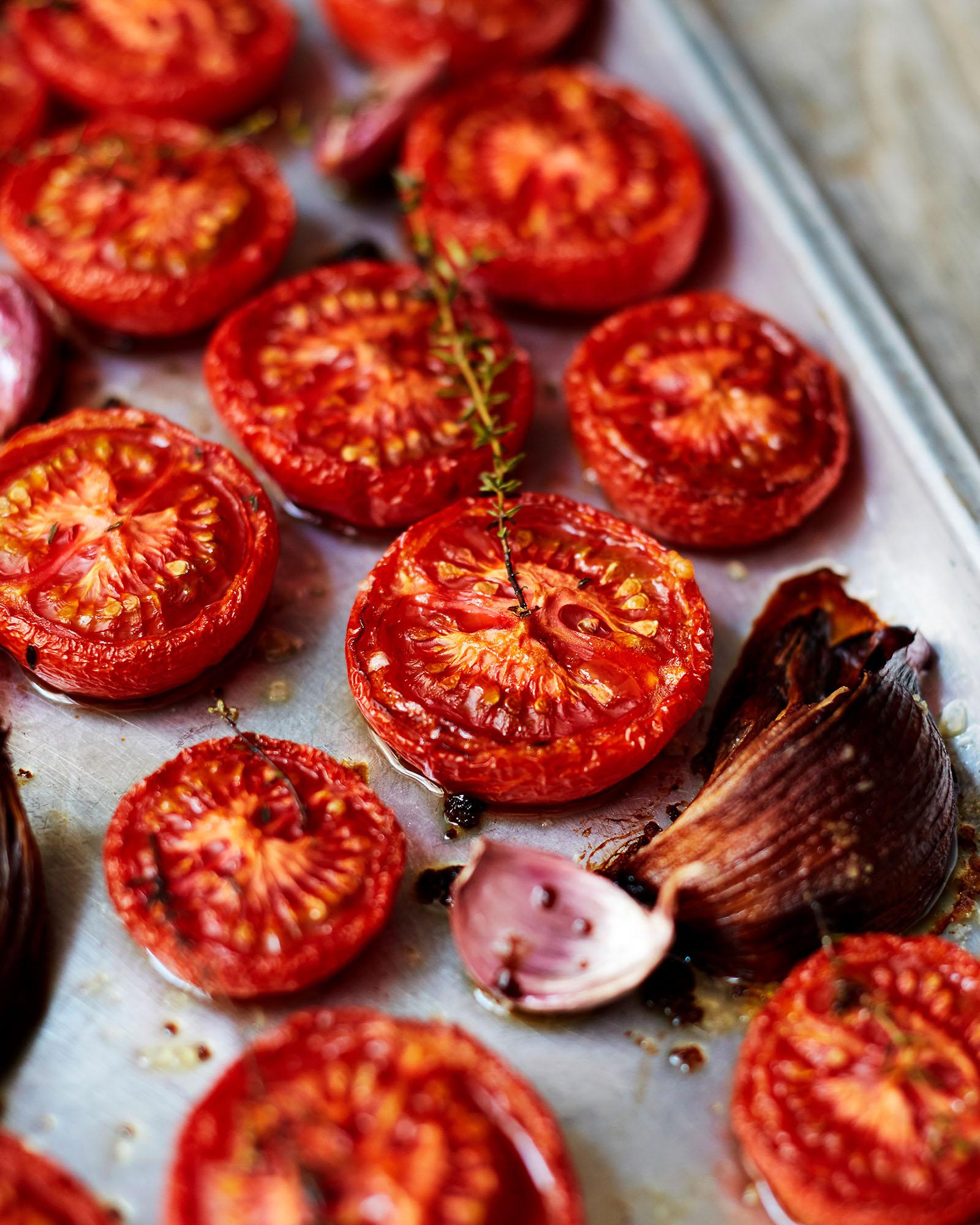 A baking sheet with roasted tomatoes, thyme, garlic cloves, and a red onion.