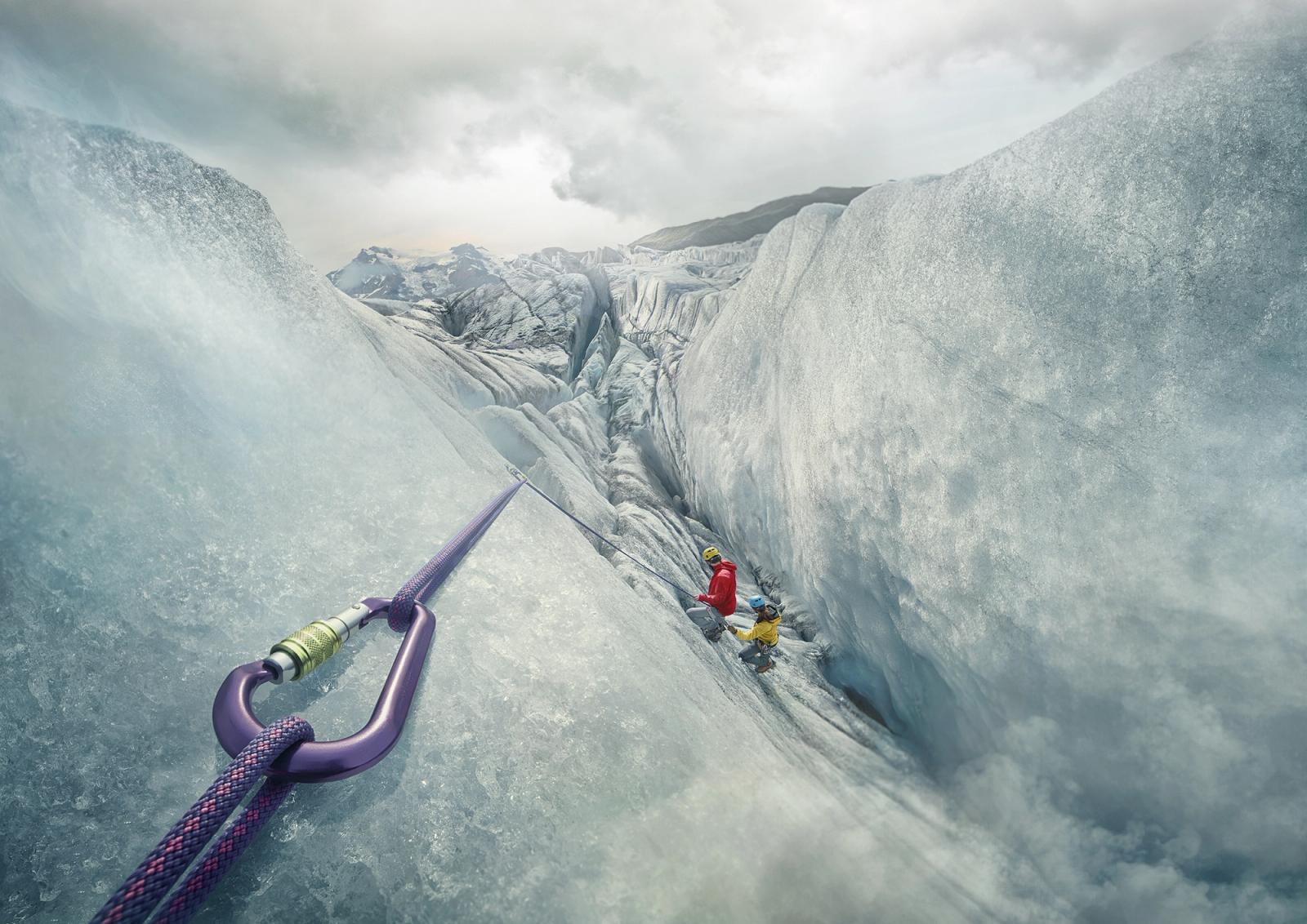 Two people wearing climbing gear and helmets are on a steep rock face with a purple and red climbing rope in the foreground.
