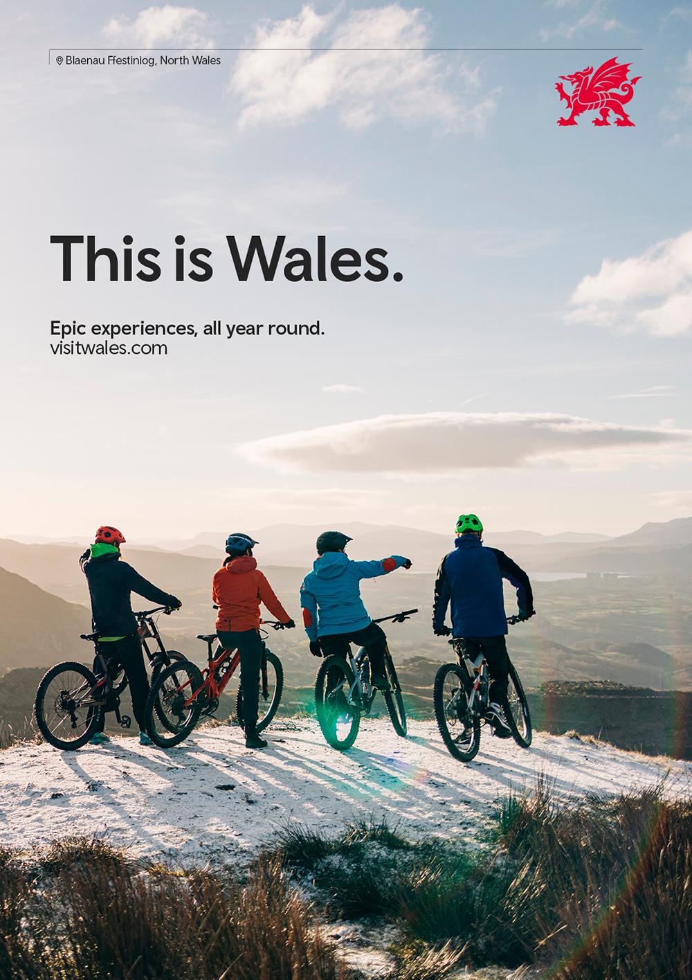 Four people on mountain bikes, wearing cycling gear, looking out at a mountainous landscape.