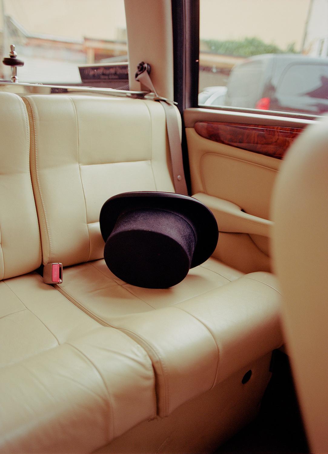 A black top hat lies on the back seat of a car, likely a luxury vehicle.
