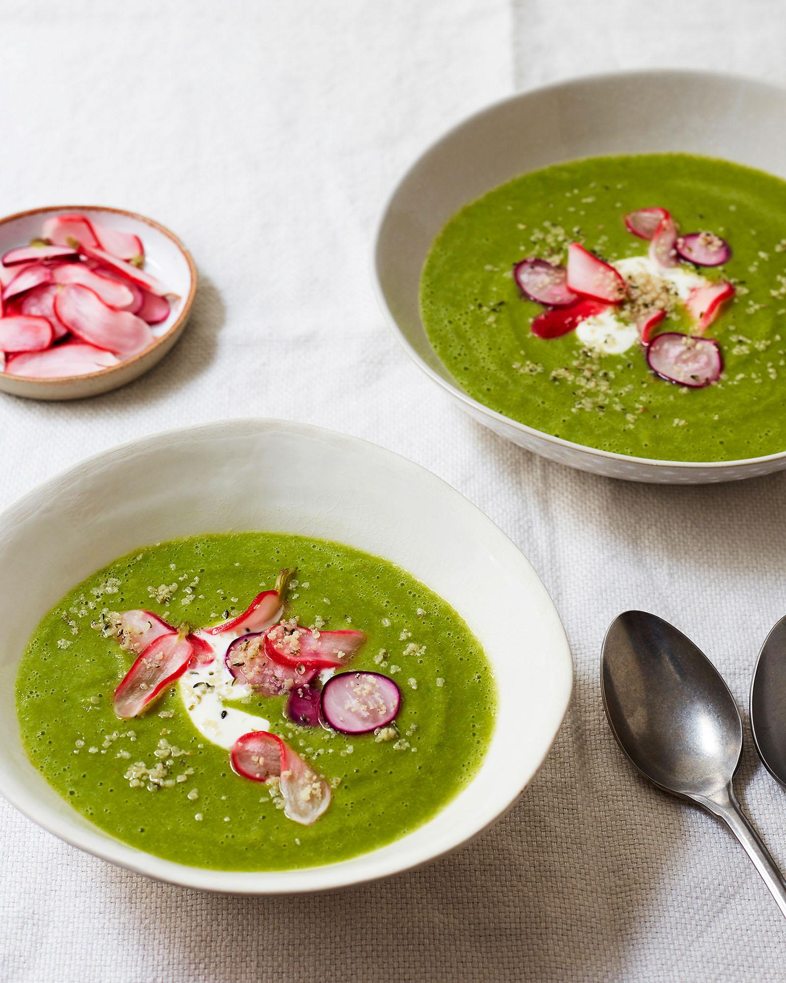 A bowl of green soup with a creamy texture, topped with sliced radishes and a sprinkle of herbs.