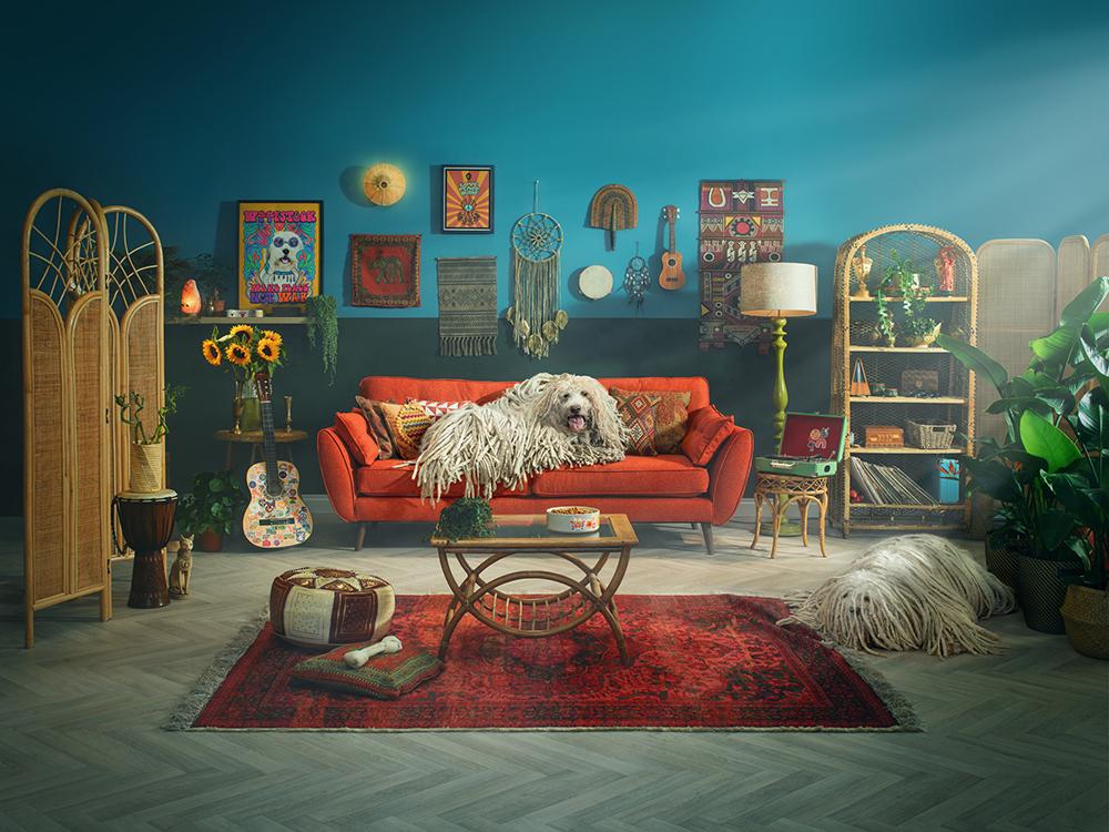 A large, shaggy, white dog is sitting on a red couch, surrounded by various objects and decorations.