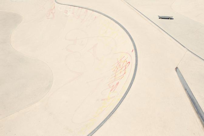 A skateboarder is riding down a concrete skatepark ramp with a smooth, curved surface and a few graffiti markings.