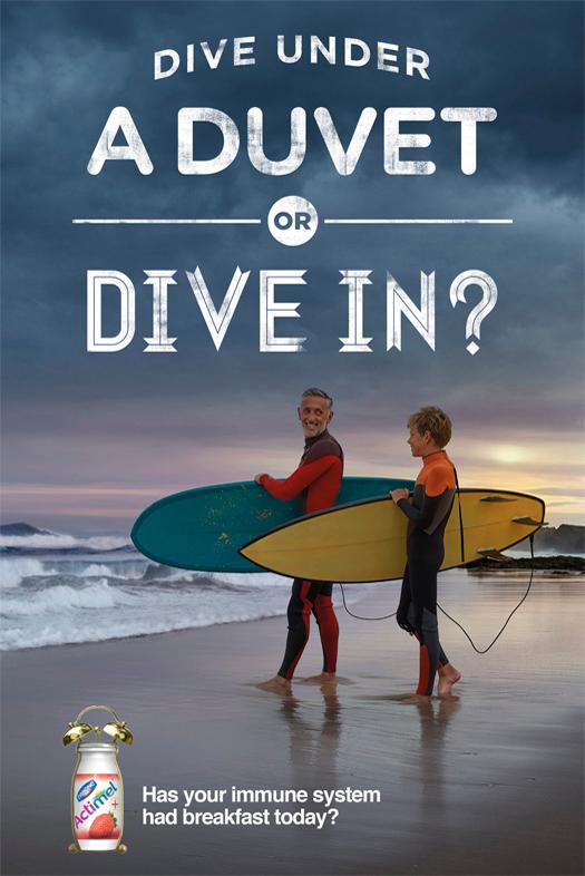 Two men in wetsuits, one holding a surfboard, standing on a beach at sunset.