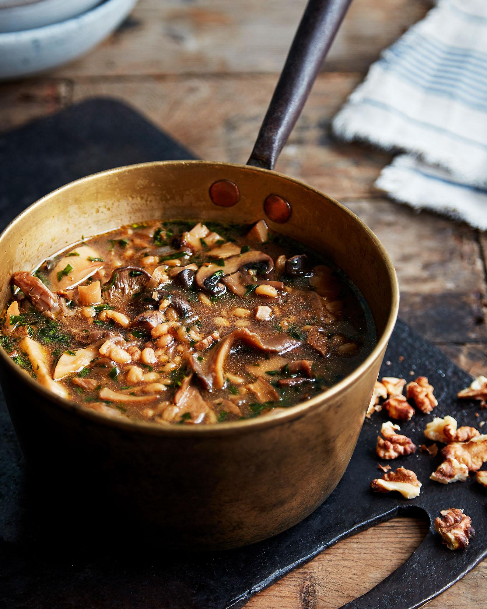 A bowl of creamy mushroom soup with a rich, dark broth and a sprinkle of fresh herbs, served in a rustic, copper-colored pot.