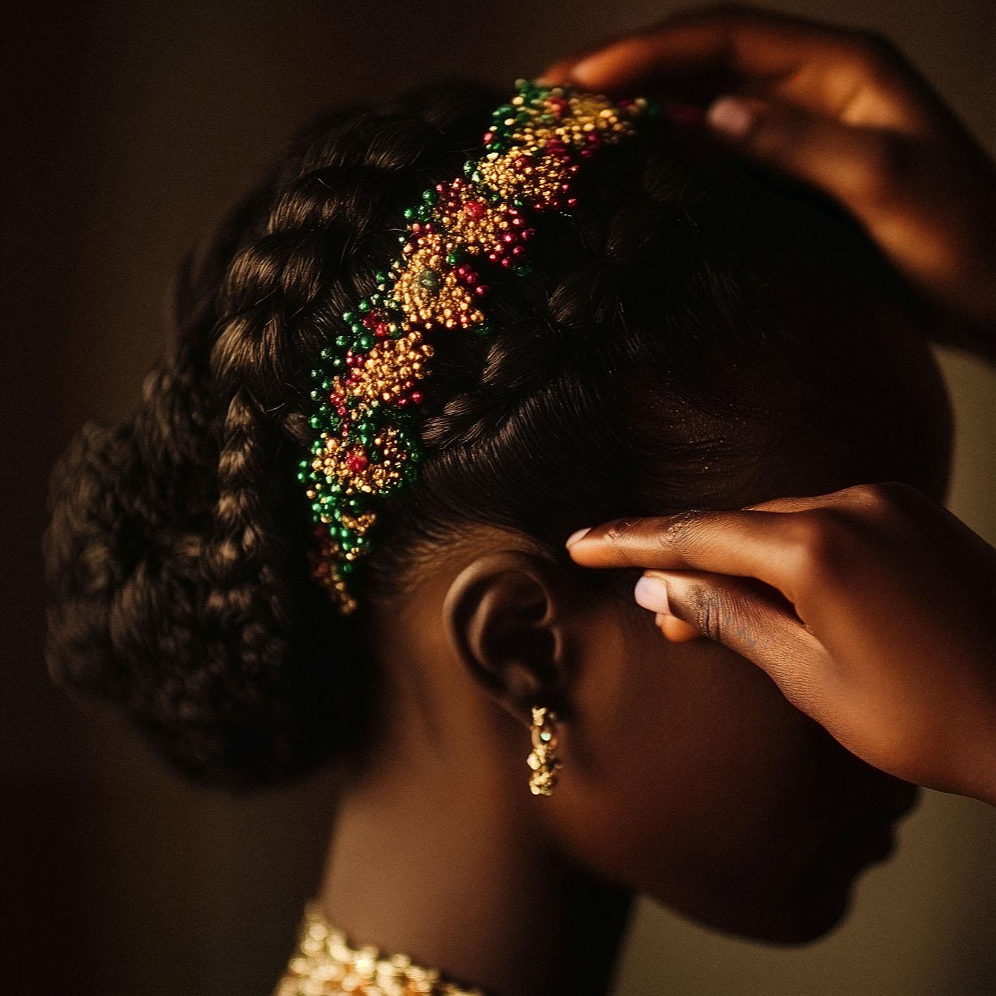 A woman's hair is being adorned with a decorative hairpiece featuring a mix of gold, red, and green beads.