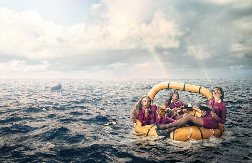 Four women in red uniforms on a yellow raft in the middle of a dark blue sea, with a shark fin in the distance.