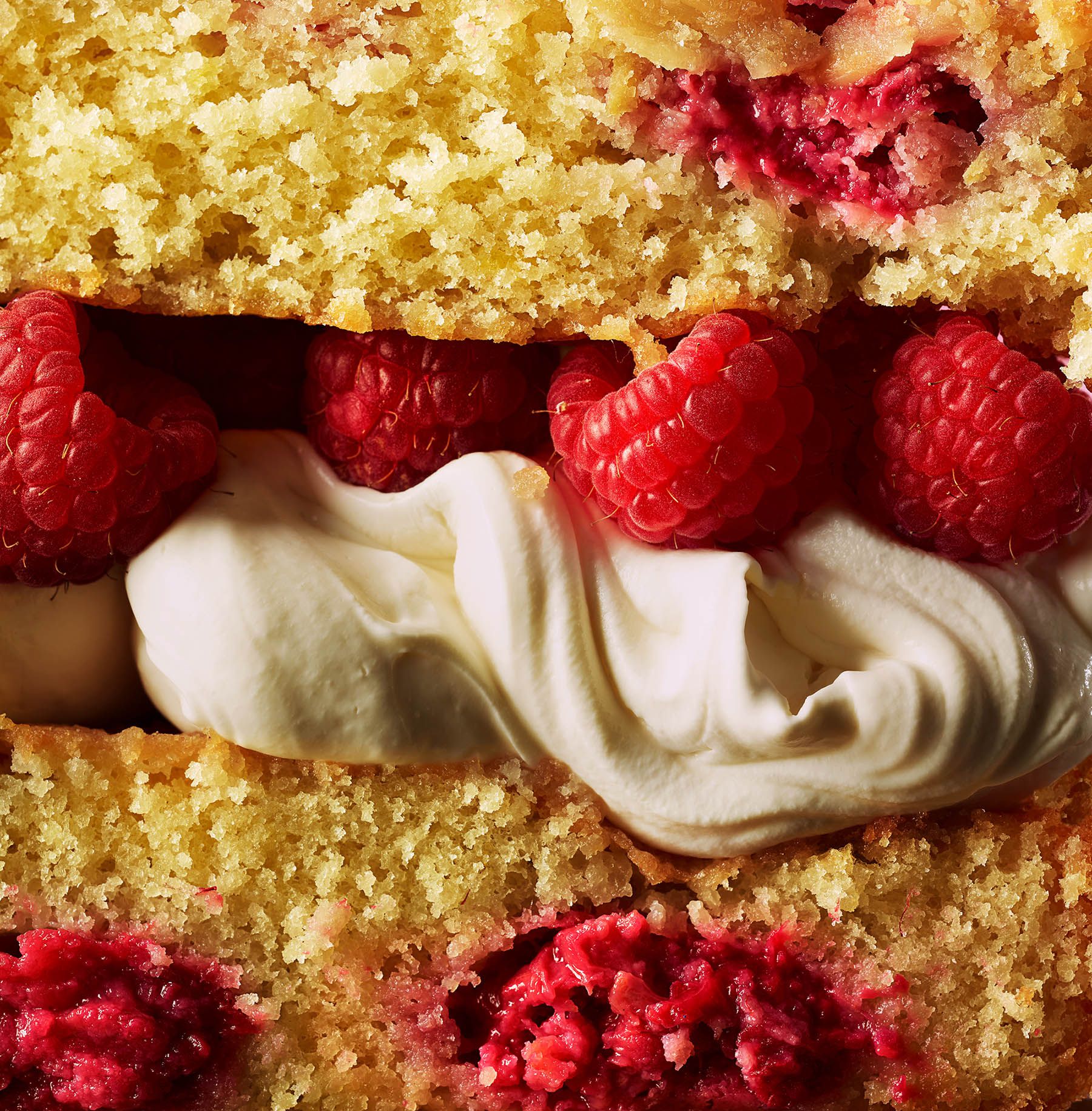 A slice of cake with cream and raspberries.