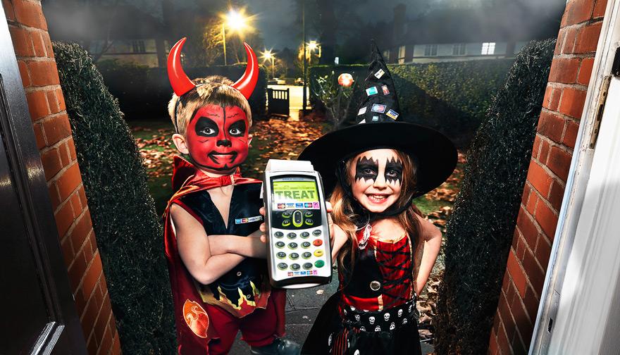 Children in Halloween costumes stand at a door with a trick-or-treat sign.