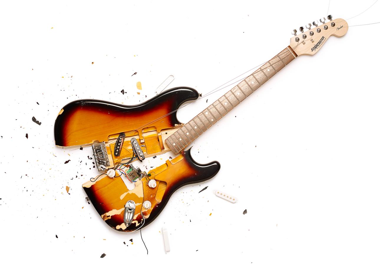 A smashed and broken electric guitar, with strings and fragments of wood scattered around it.