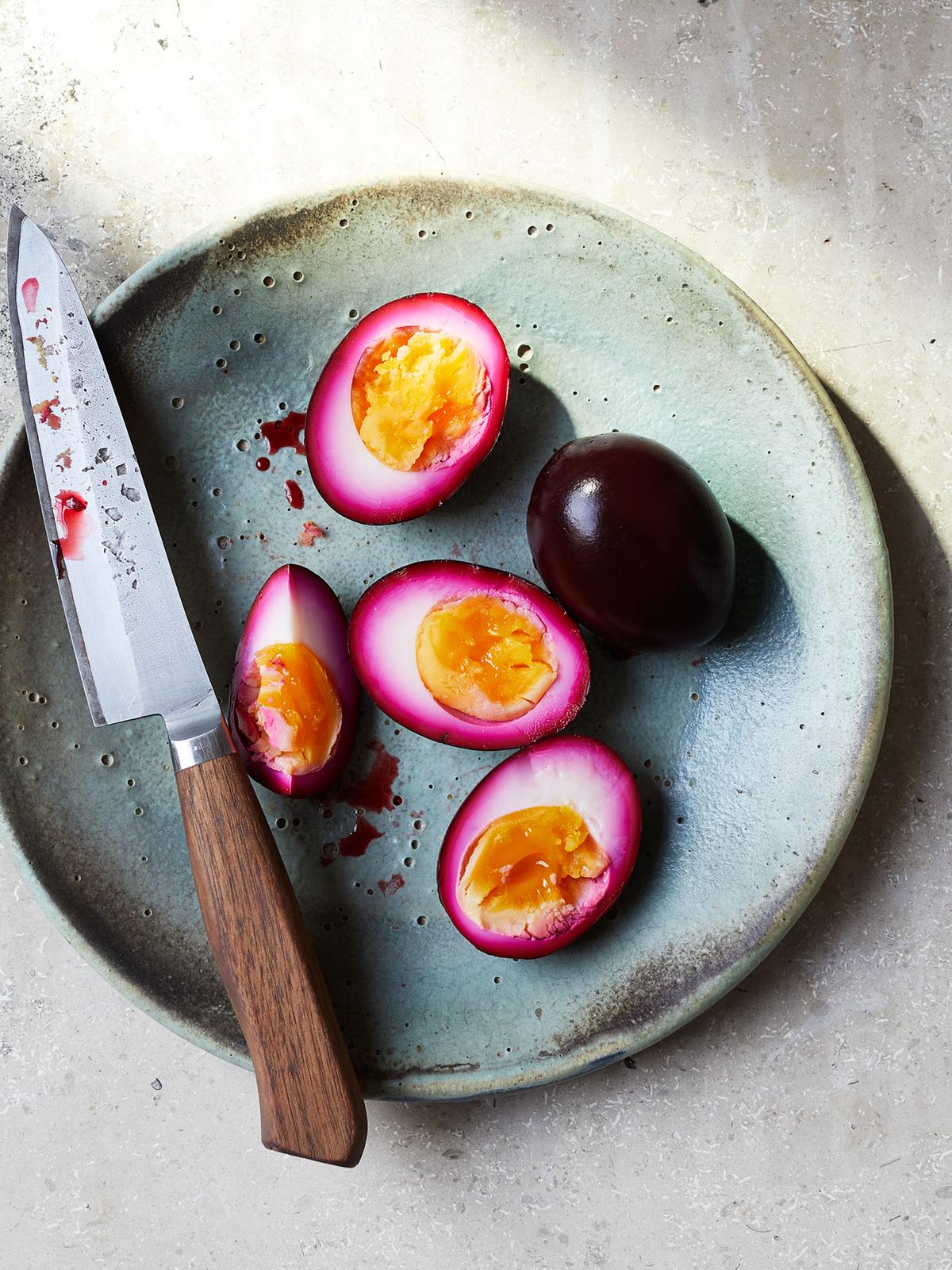 A plate of pickled eggs, with a few eggs sliced in half to show the pickled yellow centres, and a small knife with a wooden handle lying across the plate.