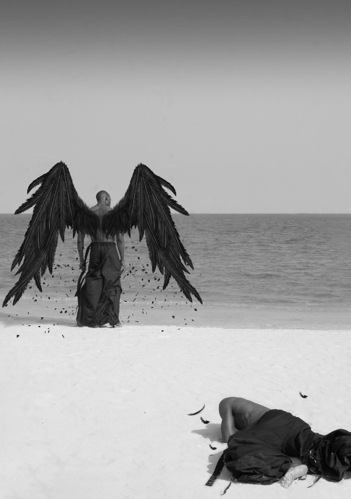 A man with black wings stands on a beach, looking out at the sea, while a woman lies on the sand, covered in black feathers.