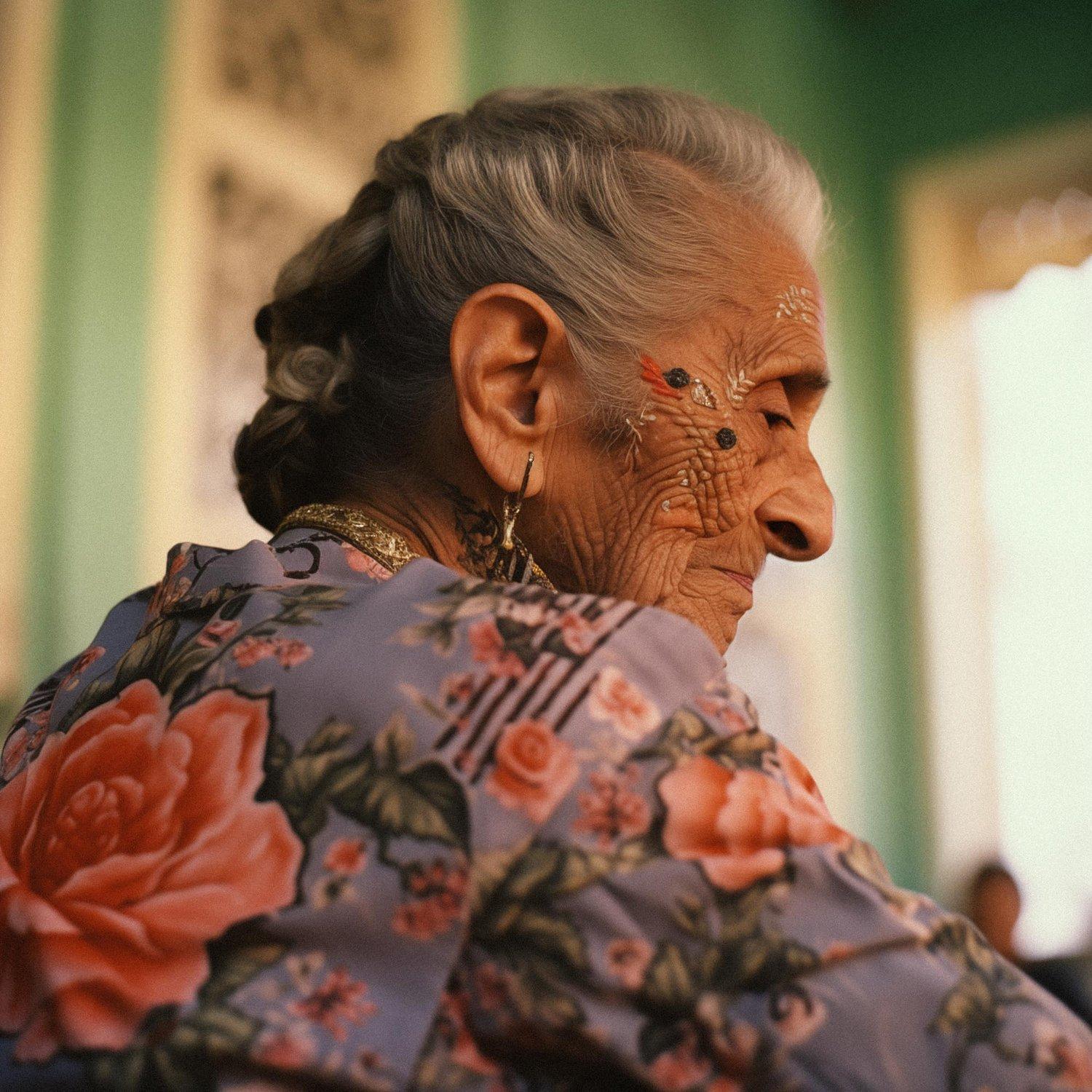 An elderly woman with a tattooed face and a floral shirt, sitting in a dimly lit room with a background of a cityscape.
