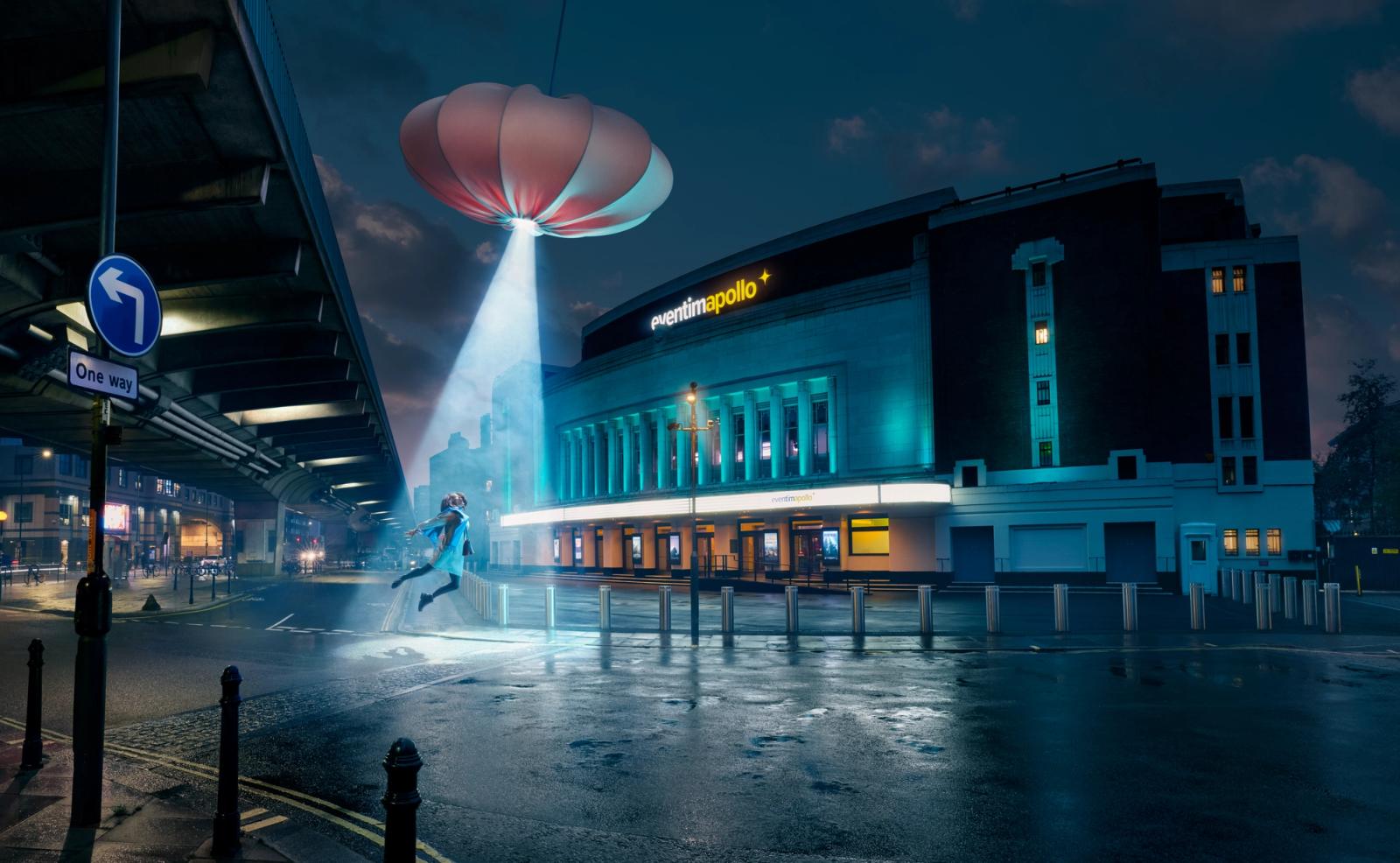 A person flying towards a hovering object in a futuristic city outside hammersmith apollo with a ufo abducting person in light
