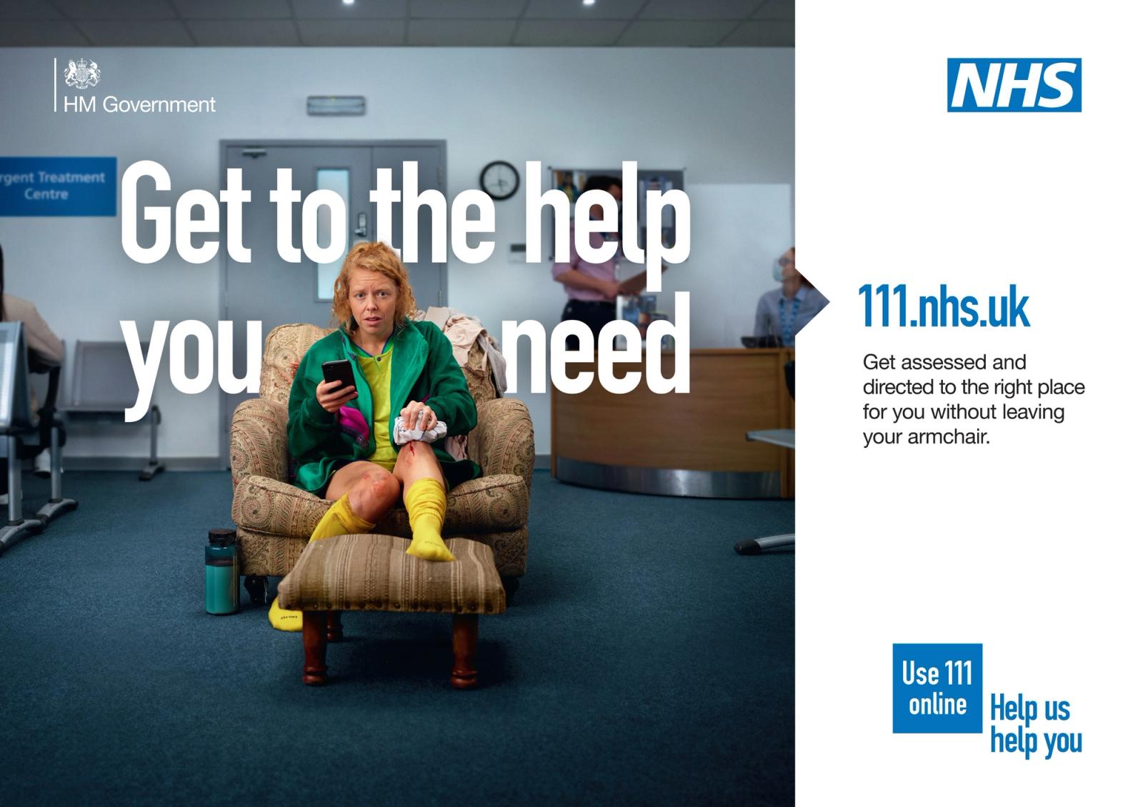 A woman in a hospital waiting room, wearing a green hospital gown, yellow socks, and a green robe, sitting in a chair, holding a phone and looking concerned.