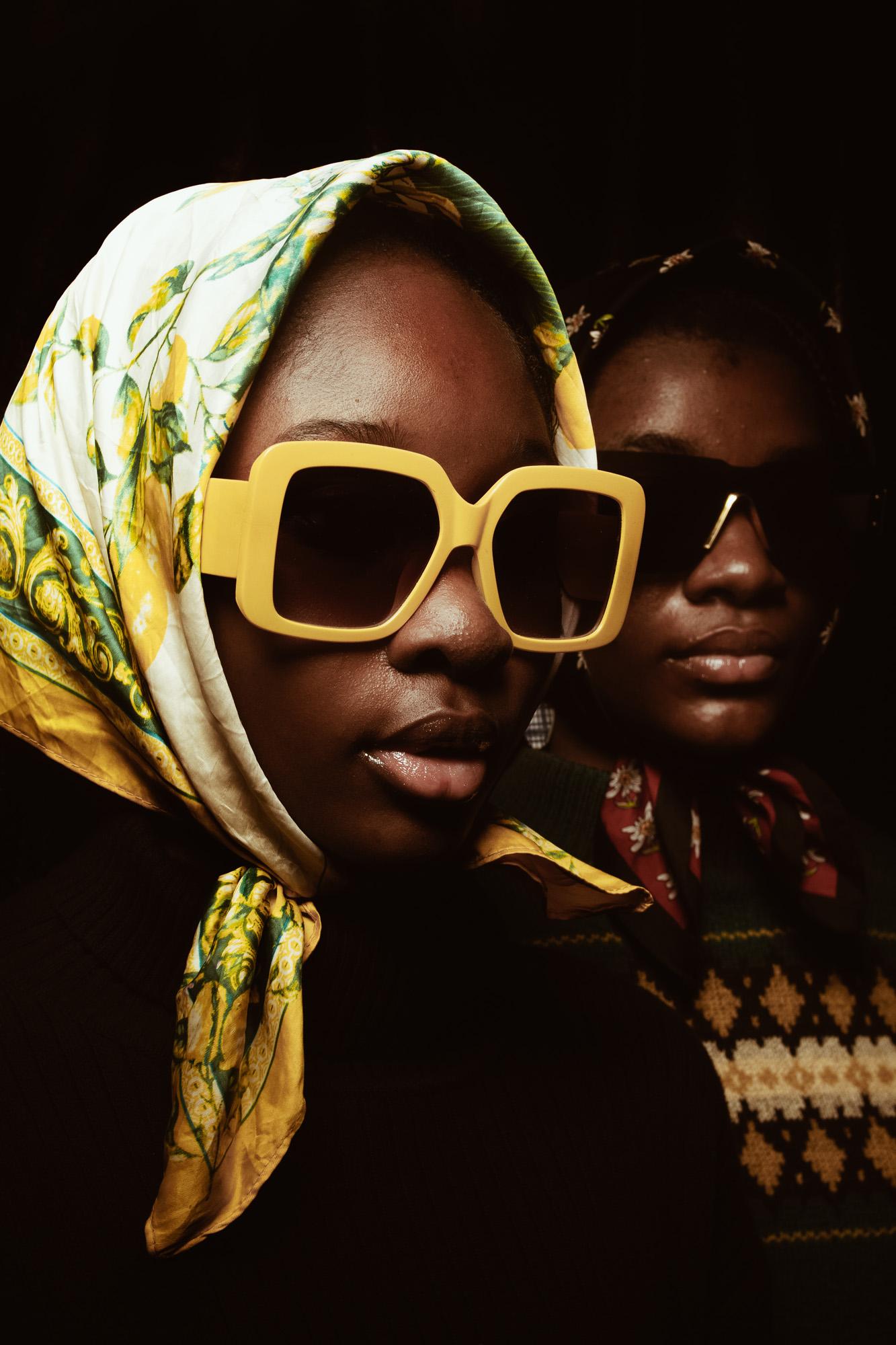 Two women in headscarves and sunglasses have serious expressions.